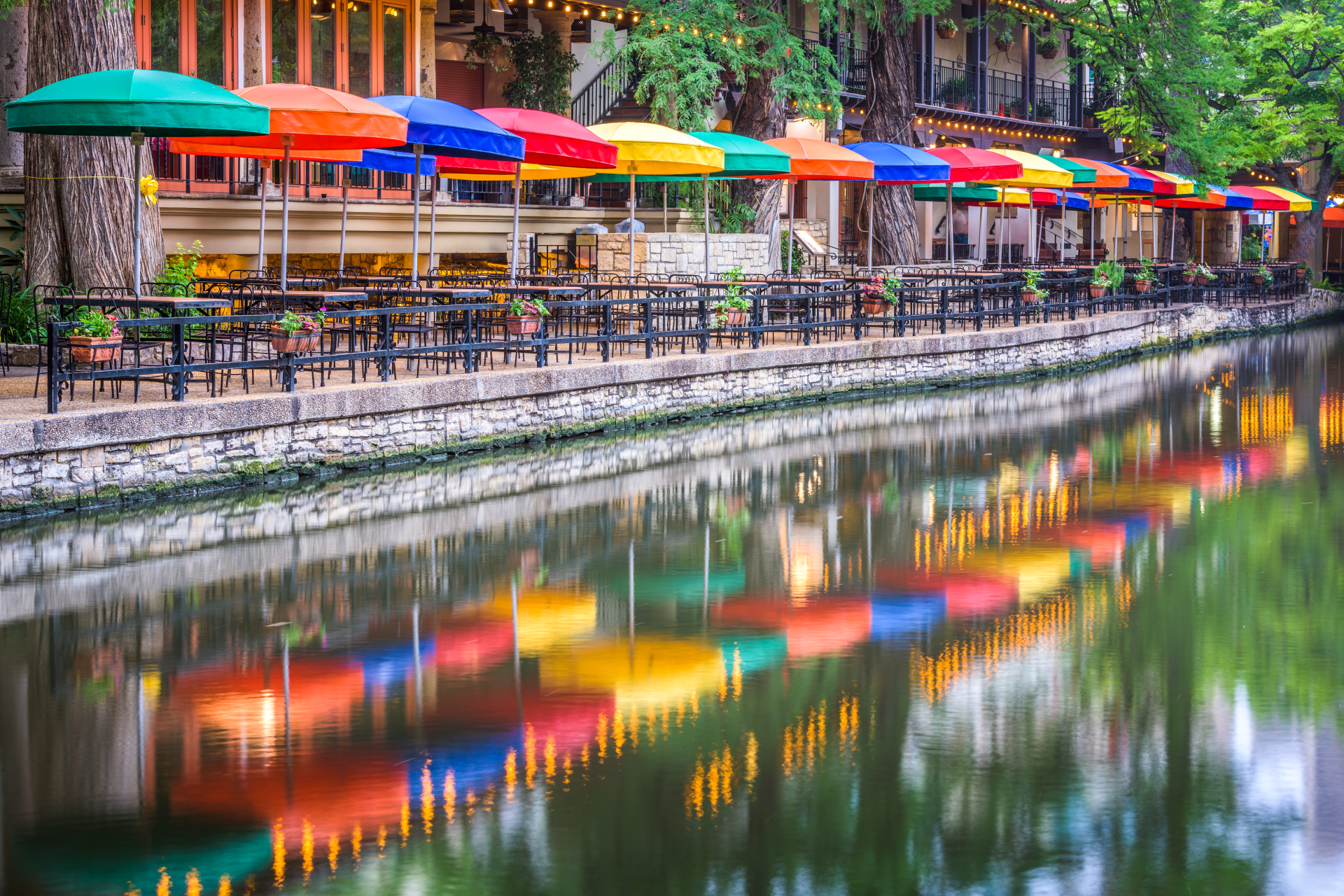 a row of tables and chairs with umbrellas by a river